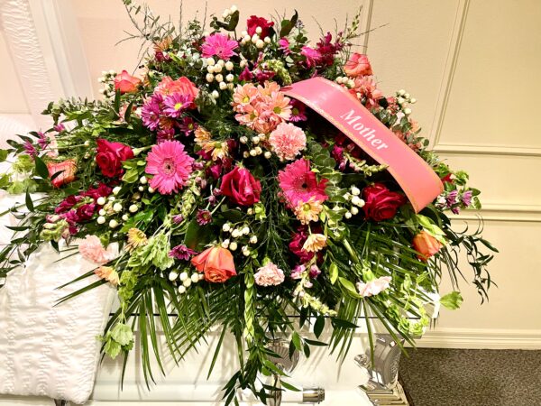 Honor a beautiful life with a pink and purple casket spray from Flowerland Florist in Sulphur Springs, TX. Featuring pink daisies, roses, carnations, and lush blooms in soft, elegant tones—perfect for funeral and memorial services. Local delivery available.