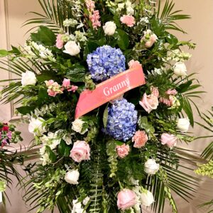 Express your sympathy with a standing easel spray featuring blue hydrangeas, pink roses, and lush greenery from Flowerland Florist in Sulphur Springs, TX. A stunning floral tribute for funerals and memorial services. Local delivery available.