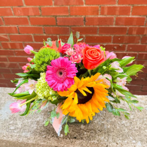 Brighten anyone’s day with “Sunshine Pop” from Flowerland Florist in Sulphur Springs, TX. This cheerful arrangement features vibrant sunflowers, pink and orange roses, yellow daisies, and fresh green accents—all designed in a compact, colorful display. Perfect for birthdays, thank-yous, get well wishes, or just because. Local delivery available.