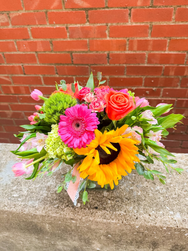Brighten anyone’s day with “Sunshine Pop” from Flowerland Florist in Sulphur Springs, TX. This cheerful arrangement features vibrant sunflowers, pink and orange roses, yellow daisies, and fresh green accents—all designed in a compact, colorful display. Perfect for birthdays, thank-yous, get well wishes, or just because. Local delivery available.